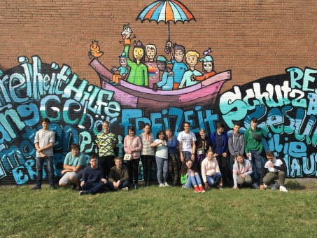 Die 17 Sch&uuml;lerinnen und Sch&uuml;ler stehen vor ihrem Graffitibild